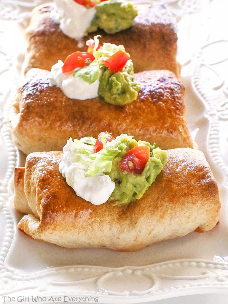 Baked Chicken Chimichangas with sour cream, guacamole, and tomato on a plate.