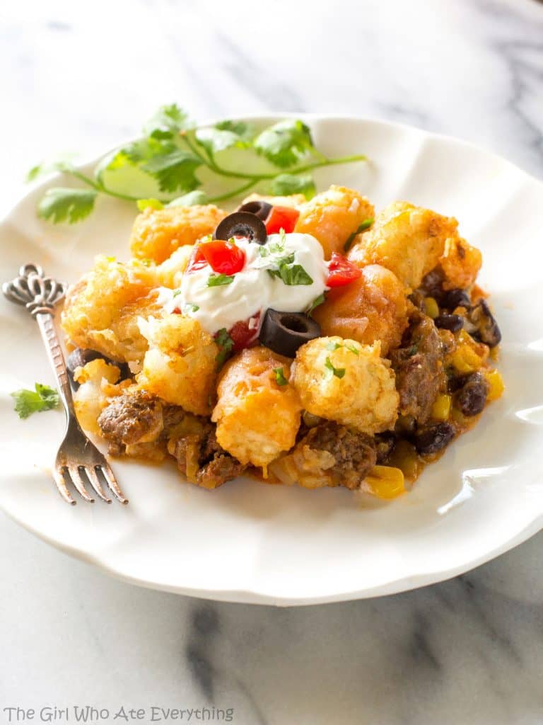 Tater Taco Casserole - A Mexican mixture of taco meat, beans, corn, and cheese topped with tater tots and enchilada sauce. the-girl-who-ate-everything.com