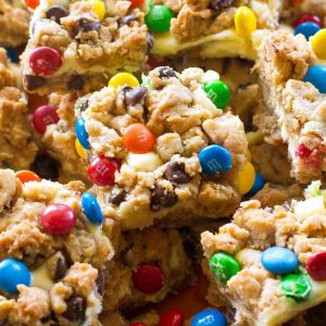 These Monster Cookie Cheesecake Bars have a layer of peanut butter, chocolate chips, oats, and M&M cookie bar with a layer of cheesecake in the middle.