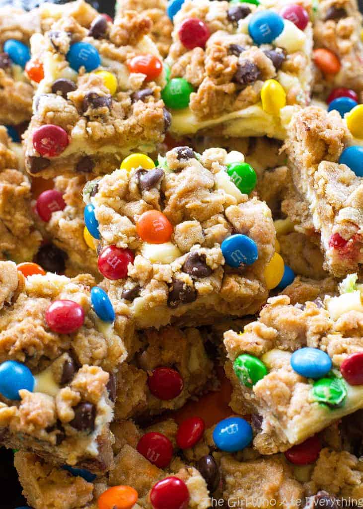 These Monster Cookie Cheesecake Bars have a layer of peanut butter, chocolate chips, oats, and M&M cookie bar with a layer of cheesecake in the middle. 