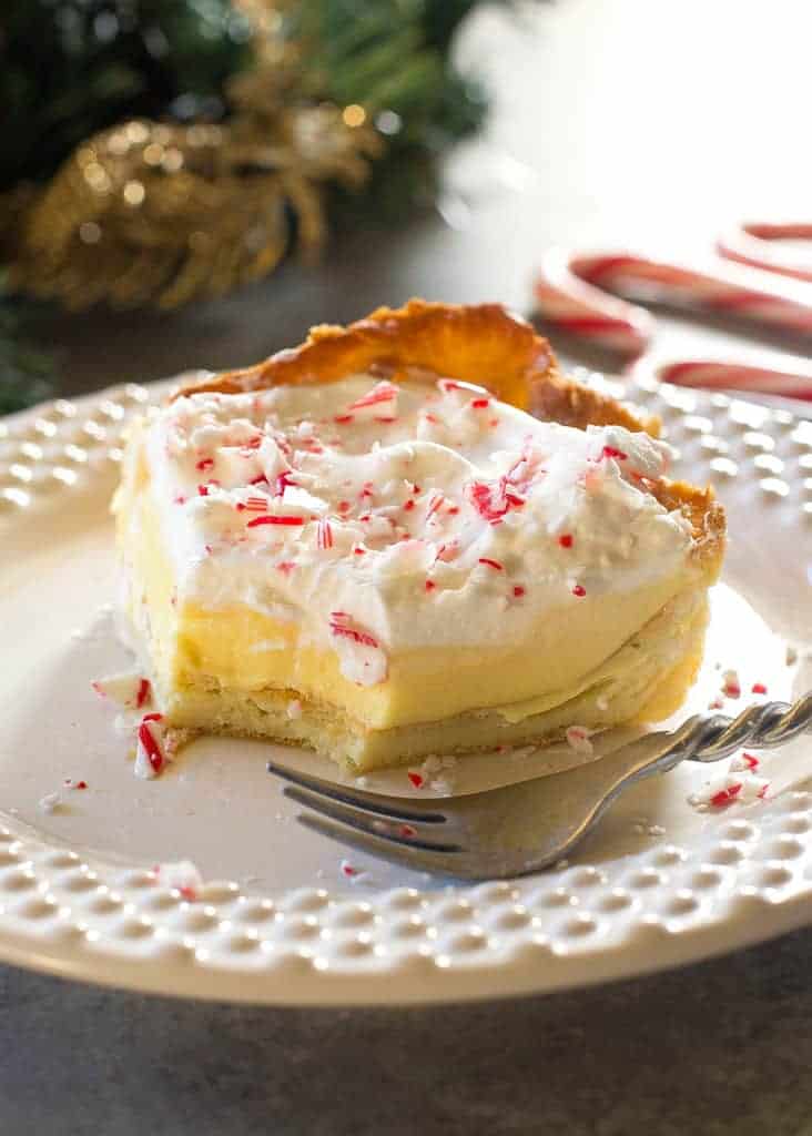 This Eggnog Éclair Cake is a unique holiday dessert with a cream puff crust, creamy eggnog layer, and topped with fresh cream and crushed peppermint candies.